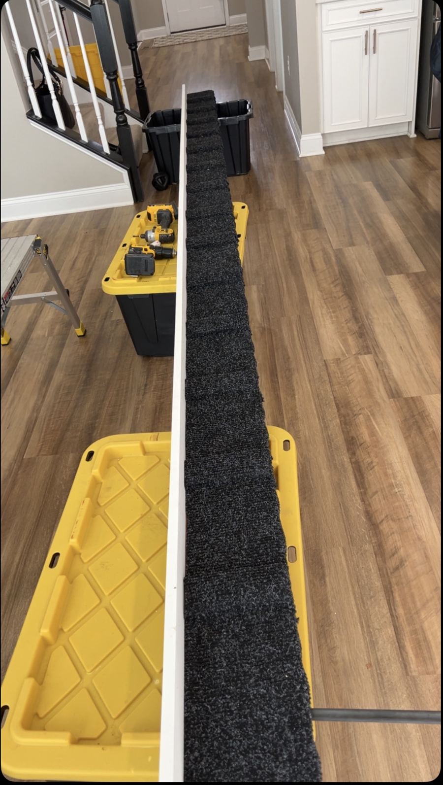 Carpeted dachshund ramp resting on yellow-lid totes indoors, with a white 1x6 PVC side rail screwed along one long edge over the wrapped carpet